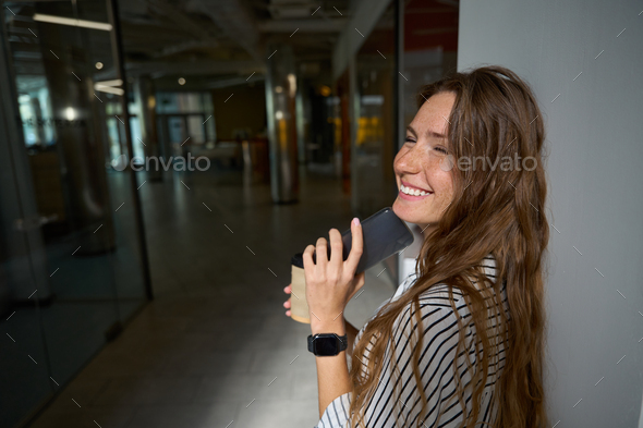 Smiling young woman standing and holding coffee, smartphone - Stock Photo - Images