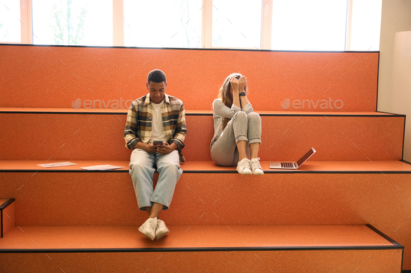 Young man using phone while lady sitting eyes closed next to him - Stock Photo - Images
