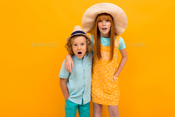 Two surprised red-haired brother and sister are looking in summer hats, are looking at the camera on