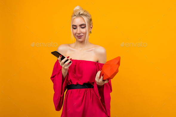 European blond girl in a red dress registers on a dating site and holds a heart made of paper