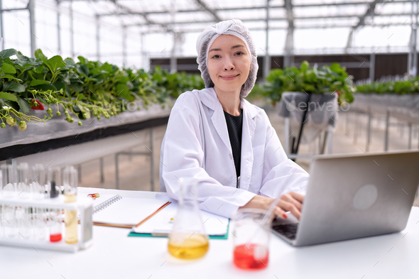 Researcher in greenhouse farming lab take sample of flower and leave and key information to laptop