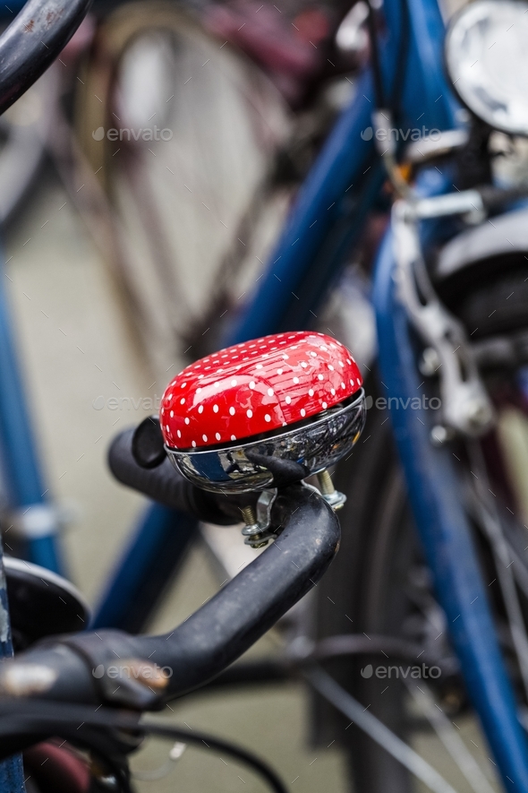 Vertical close shot of a red bicycle bell on the handle with a blurred background