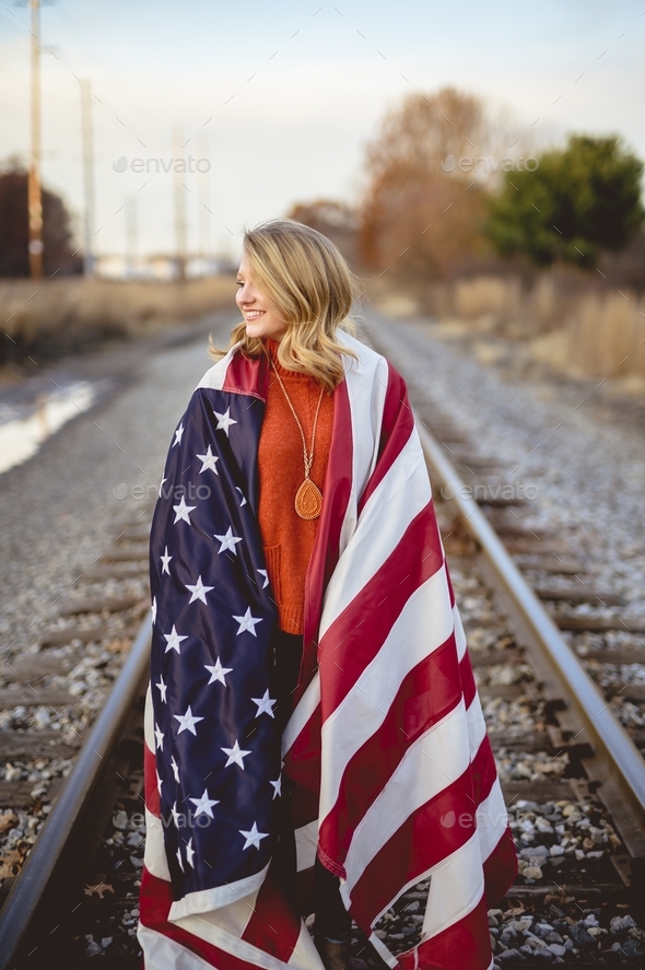 Vertical shot of a female with the American flag on her shoulders standing on the railway