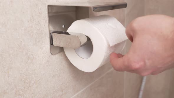 Men's Hands Unwind and Tear Off a Short Piece of Toilet Paper alt