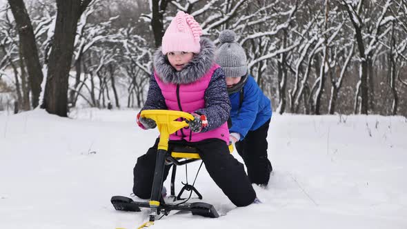 Little Boy Rides a Girl on a Sled in Winter in a Snowcovered Forest alt