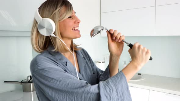 Positive blonde woman Having fun, singing loudly in kitchen using ladle as microphone.