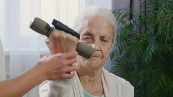 Elderly Woman Doing Dumbbell Curls with Help of Female Volunteer