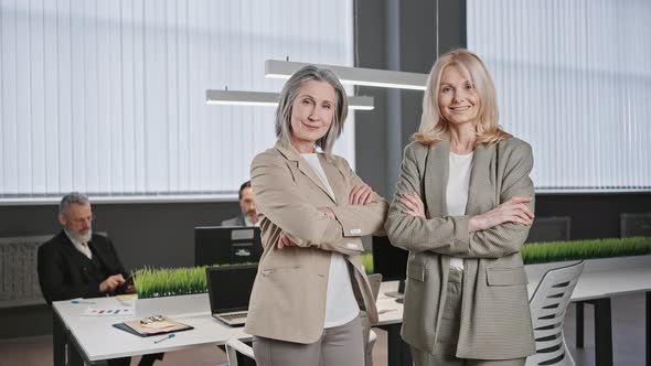 Zoom Out Portrait of Two Confident Mature Ladies Smiling to Camera Posing at Office with Folded alt