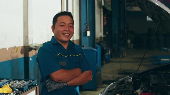 Professional car mechanic looking at camera and smiling at repair service station. alt