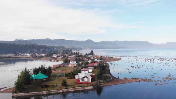 houses on peninsula surrounded by still beautiful blue sea drone flying backwards