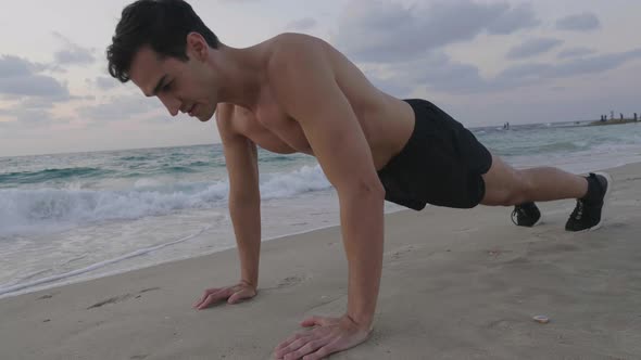 Handsome young male doing push up exercise on beach alt