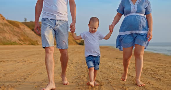 Happy Child Walks on the Sand with His Parents Steps on the Sand with Bare Feet