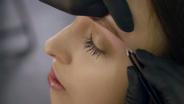 Indoor Close-up of a Makeup Master Carefully Plucking Eyebrows with Tweezers alt