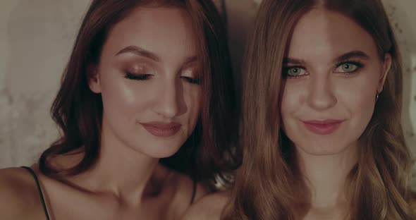 Two Pretty Girls Close Open Eyes and Look Into Camera with Flirting Smile alt