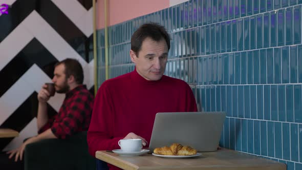 Handsome Middleaged Man Messaging and Chatting Sitting with Laptop in Cafe