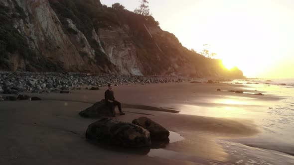 A man sitting in peaceful meditation and present awareness on a sandy beach with ocean waves at sunr alt