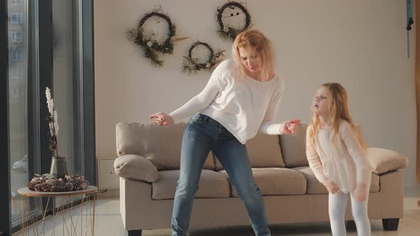 Active young mom babysitter and cute little kid daughter jumping dancing in modern house living room