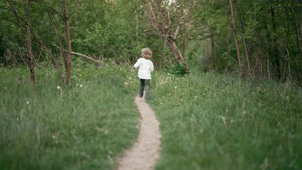 Little Ukrainian Boy Cheerfully Running Along Path on Forest Lawn or in Park alt