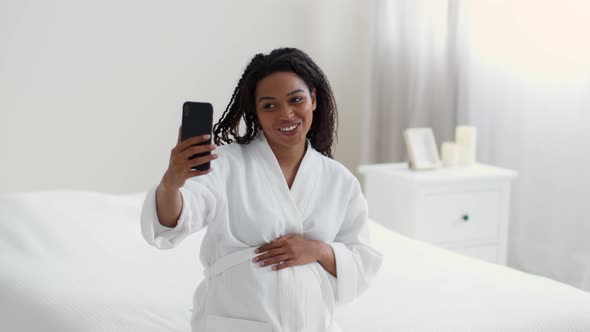 Young Happy African American Woman Woman Video Chatting with Friends Via Smartphone Sitting on Bed alt