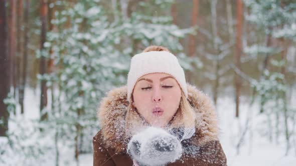 Beautiful Woman in Winter Clothes Blowing Snow From Her Hand