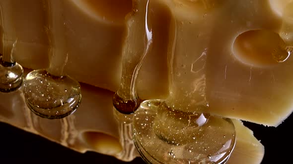 Drops of honey flow down from the cheese on a mirrored black background. alt