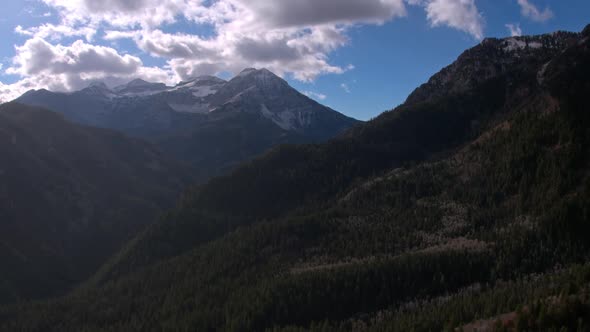 Aerial view moving over mountain layers towards a snow capped peak alt