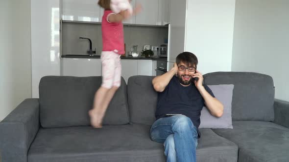 Happy Little Girl Interferes with Her Fathers Work Jumping on Couch and Plays alt