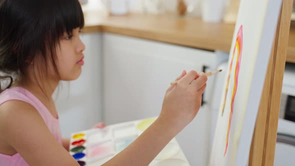 Asian young happy kid girl coloring on painting board in living room. alt