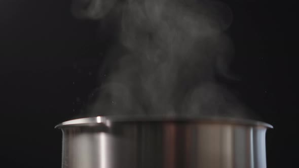 Slow Motion Closeup of Steam Rising From Steel Pot Over Black Background alt