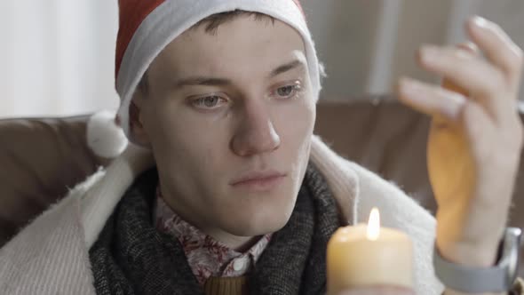 Headshot of Lonely Young Caucasian Man in New Year Hat Blowing Out Candle alt