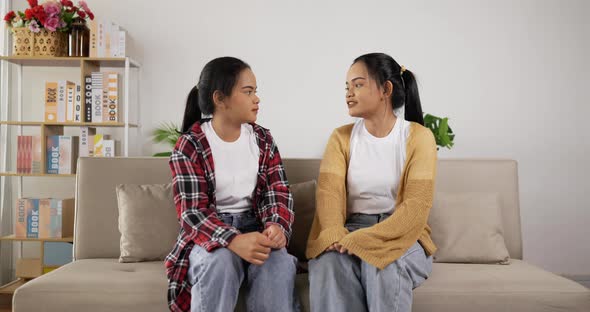 Sad young twin girls sit back to each other after a quarrel with her twin sister. alt