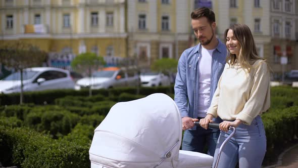 Smiling Young Parents Walking in City Garden Pushing Newborn Pram, Parenting alt