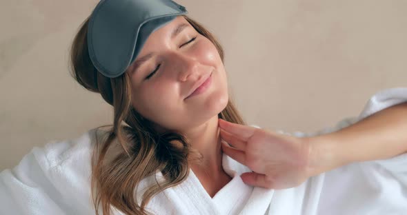 Happy Woman in Bathrobe Puts on Blindfold Sitting on Bed alt