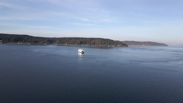 Fall colors dot the shoreline as a vessel ferry crosses calm blue waters, aerial alt