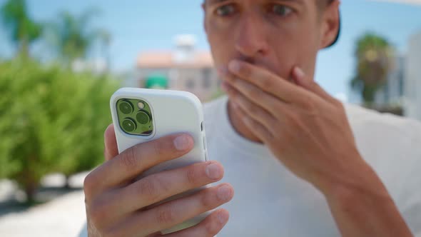 Closeup of Shocked Man Reading Bad News on His Smartphone While Standing Outdoors