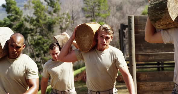 Military troops carrying heavy wooden logs during obstacle course alt