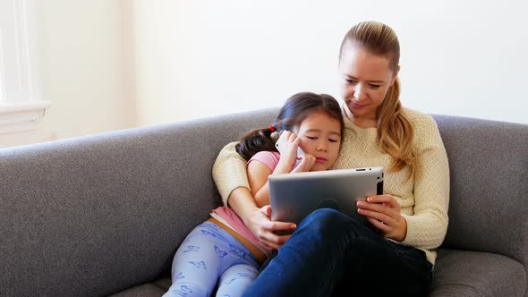 Mother and daughter using digital tablet in living room alt