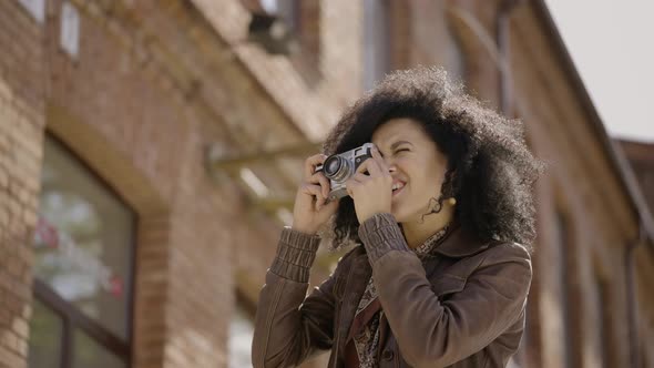 Stylish Young African American Woman Walking Street and Taking Pictures with Retro Camera alt