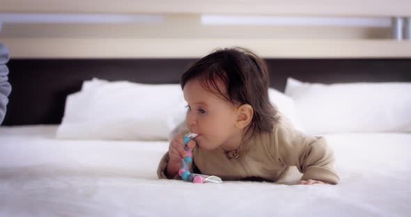 Baby Lies on Her Stomach on the Bed in the Nursery and Licks the Nipple Holder alt