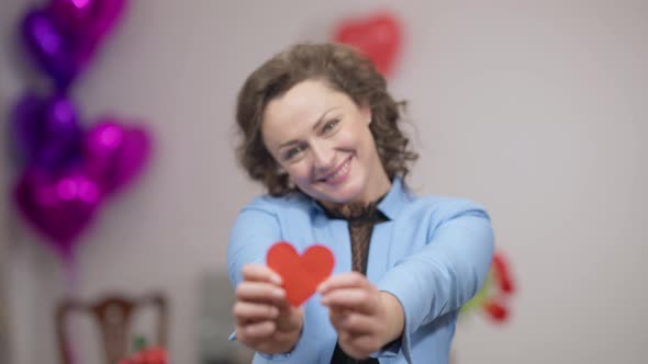 Rack Focus From Smiling Happy Face of Beautiful Caucasian Woman to Female Hands Holding Red Paper alt