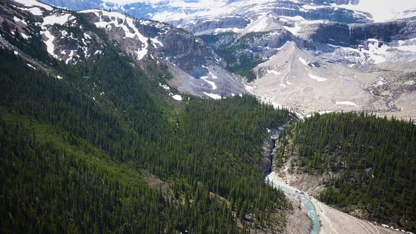 Cinematic aerial view of the forest and snow covered Rocky Mountains. alt