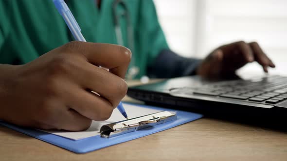 Black Doctor Works at a Computer and Makes Notes in His Office. Close Up of Doctor Hands. alt