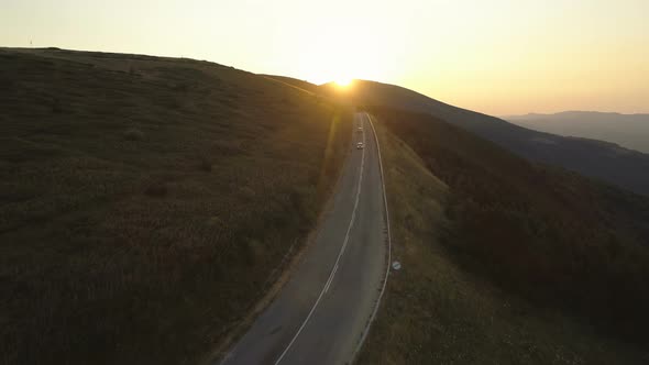 Two Cars Driving Along a Mountain Pass in the Evening at Sunset alt