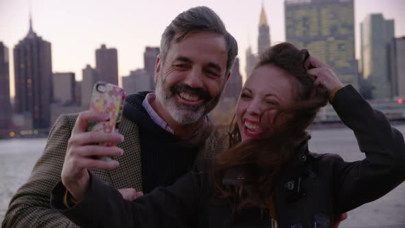 Couple in New York City taking cell phone selfie with city skyline in background