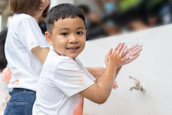 Asian boy washing hands with soap on outdoor wash basin after painting color by his hands at school