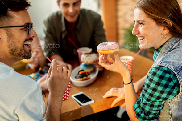 Happy couple talking while eating donuts with friends in a cafe,
