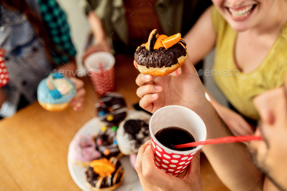 Close-up of man drinking juice while eating donut with friends in a cafe.