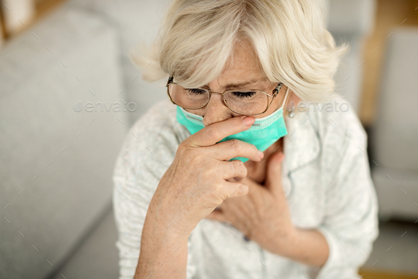 Sick mature woman with face mask coughing at home.