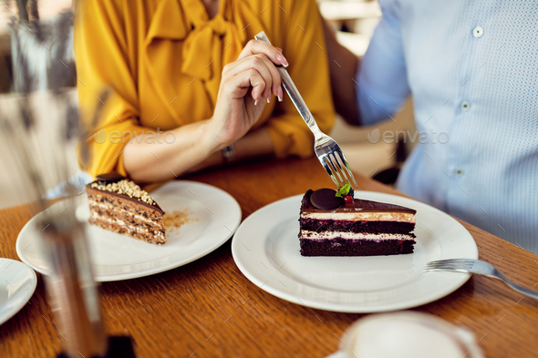 Close-up of a couple sharing a cake in a cafe.