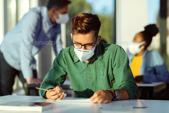 College student wearing protective face mask while writing exam in the classroom.